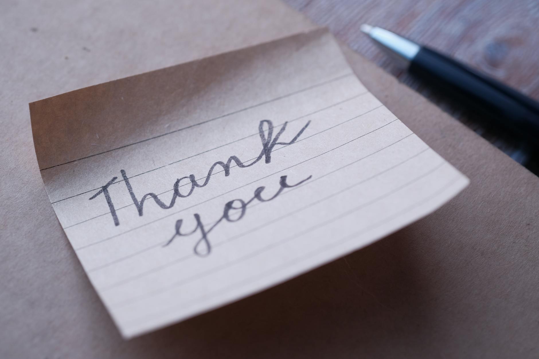 A handwritten thank you note on lined paper next to a pen