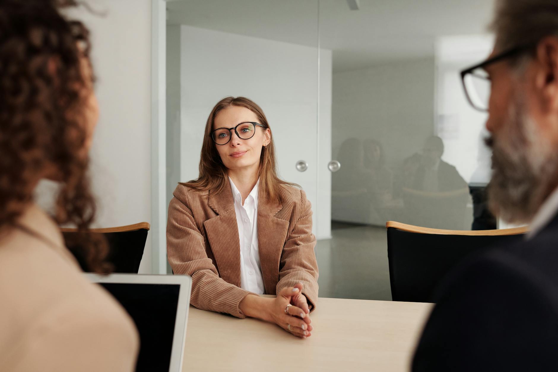 A woman in a corduroy blazer and glasses sitting across a table from two interviewers