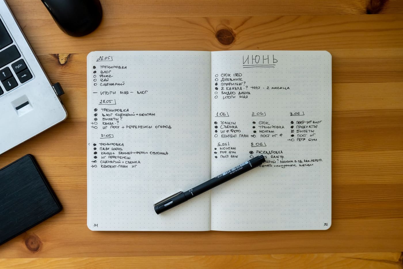 An open notebook with a bullet list and a black pen on a wooden desk beside a laptop