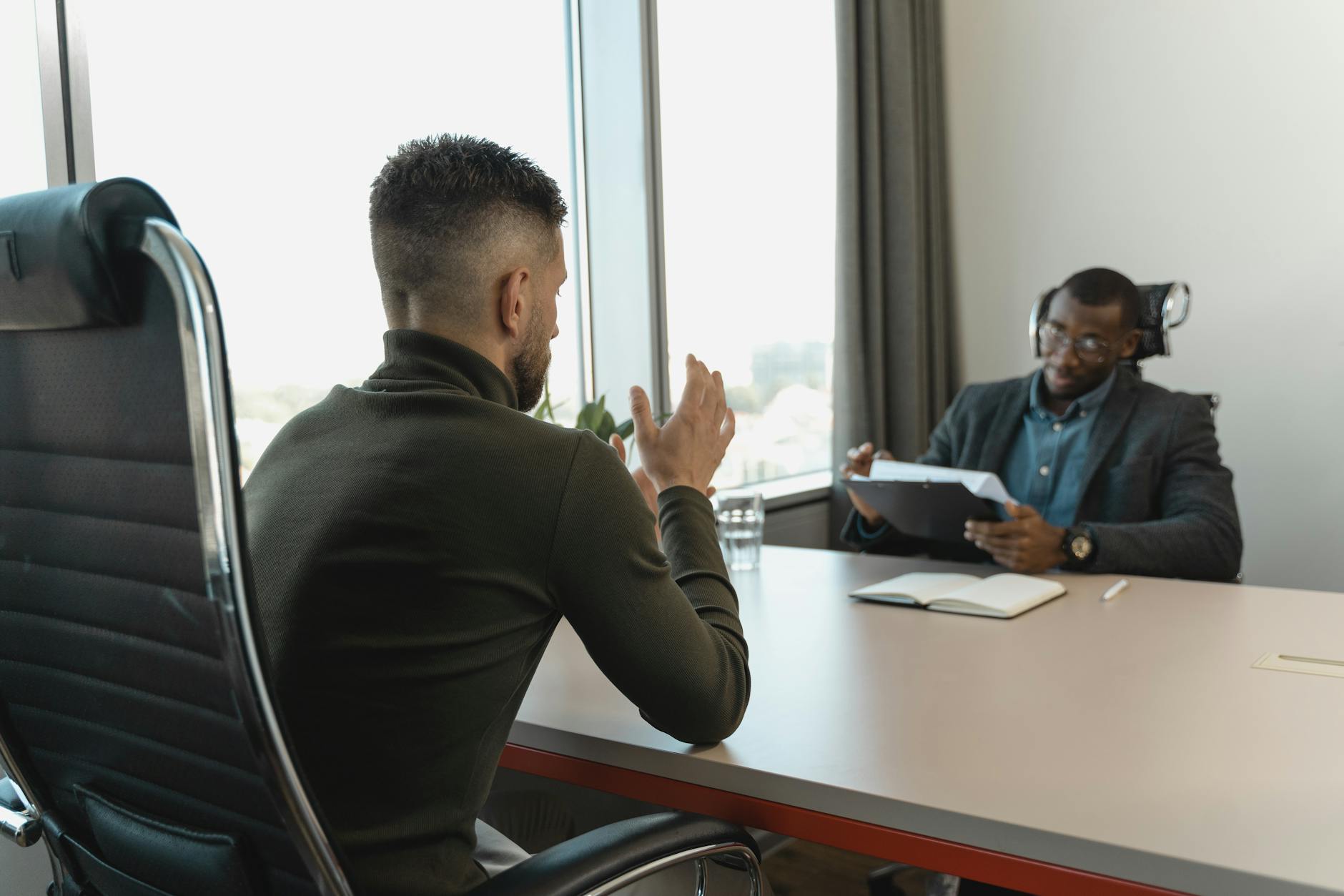 Two people in a bright office talking across a table during a job interview